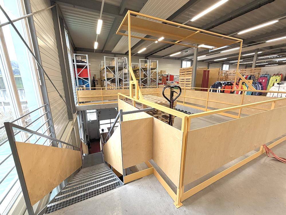 Detailansicht des Treppenabgangs und einer Ladezone mit Hubwagen in der Lagerhalle.
