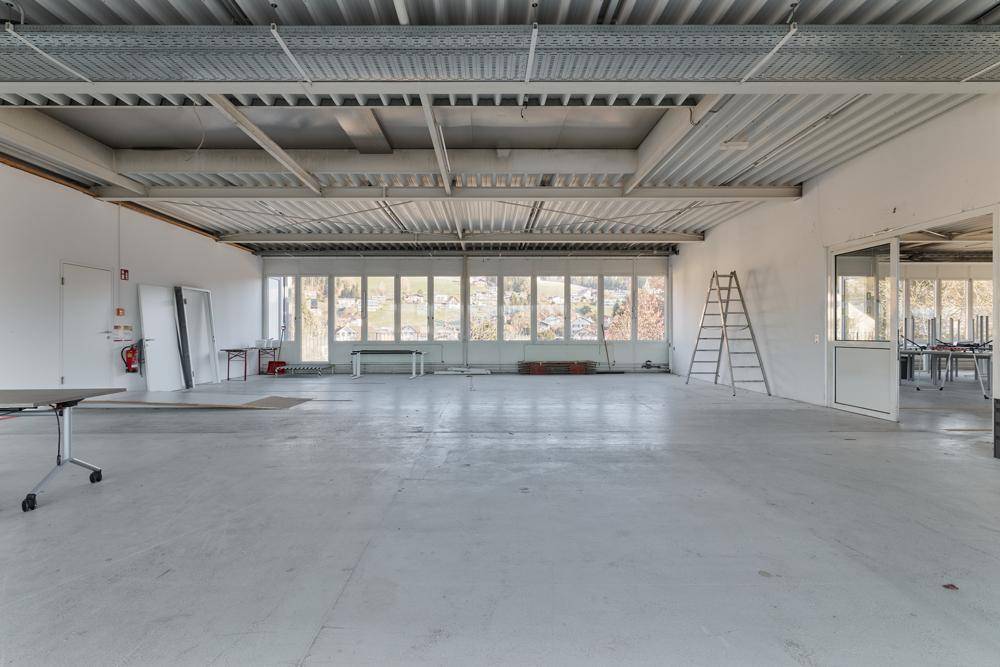 Geräumige Halle mit hohen Decken, großen Fenstern und Betonboden, bereit für die Nutzung.