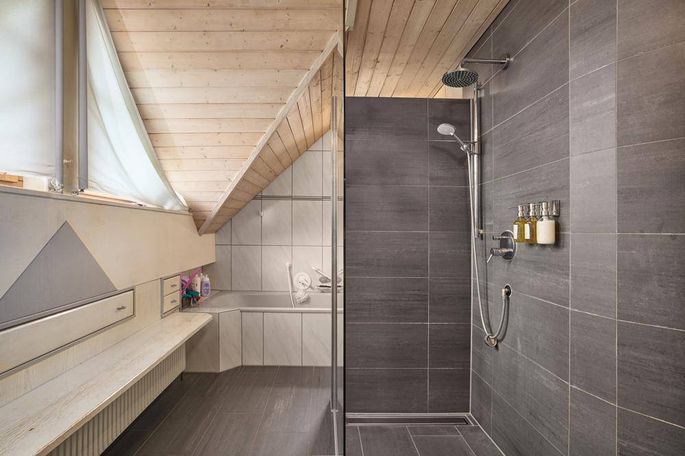 Modernes Badezimmer mit begehbarer Dusche, Badewanne und schräger Decke.