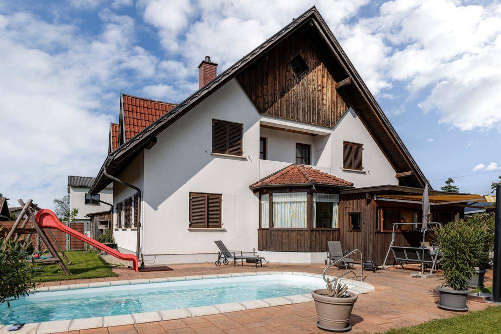 Charmantes Einfamilienhaus mit Satteldach, Holzverkleidung, Garten und privatem Swimmingpool.
