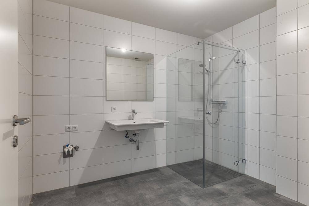 Modernes Badezimmer mit weißen Fliesen, ebenerdiger Dusche und einem einzelnen Waschbecken.