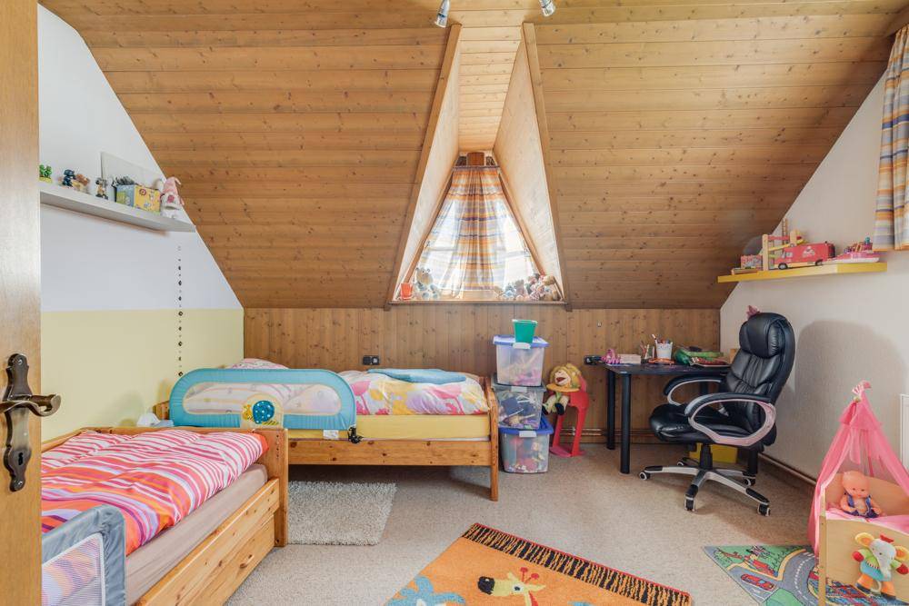 Kinderzimmer im Dachgeschoss mit Holzdecke, Dachschräge und Spielbereich am Fenster.