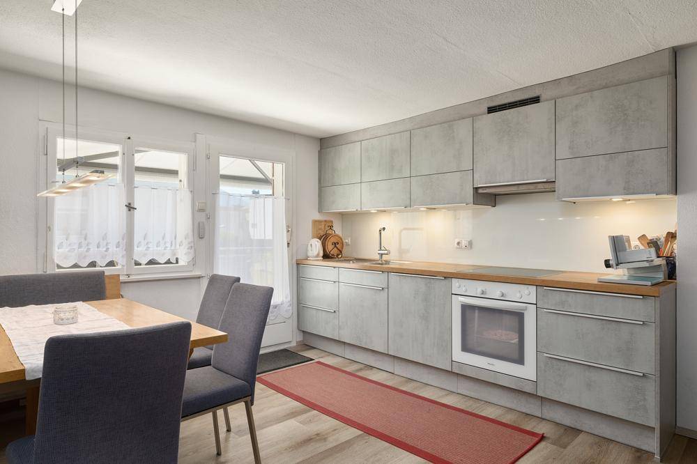 Moderne Küche mit grauen Fronten, Holzarbeitsplatte und Essbereich am Fenster.
