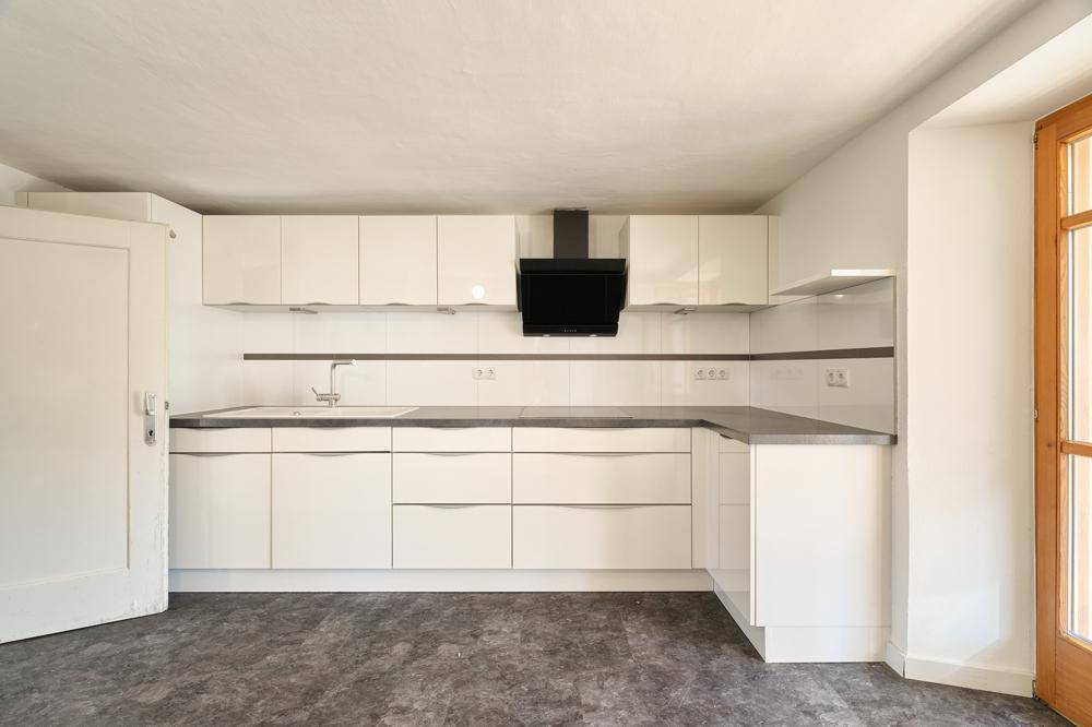 Moderne Küche mit weißen Hochglanzfronten, dunkler Arbeitsplatte und Dunstabzugshaube.