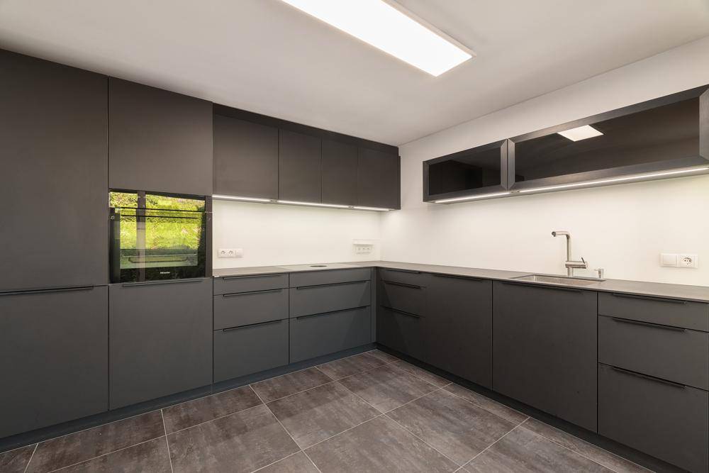 Moderne Küche mit grauen Schränken, integrierten Geräten und Fliesenboden.