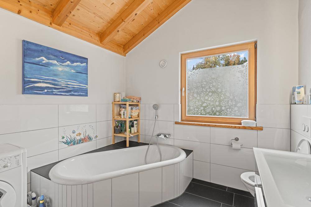 Helles Badezimmer mit Badewanne, Fenster und Holzdachschräge.