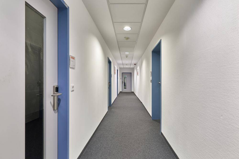 Langer, gut beleuchteter Büroflur mit Teppichboden und mehreren Türen zu den Büroräumen.