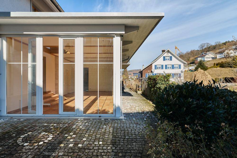 Moderner Glasanbau am Haus mit gepflastertem Weg und Blick auf die Umgebung.