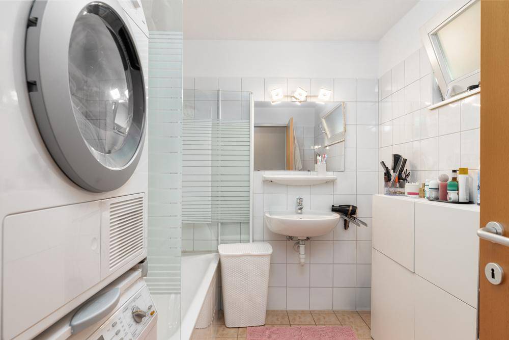 Helles Badezimmer mit Badewanne, Waschbecken, Waschmaschine und Trockner.