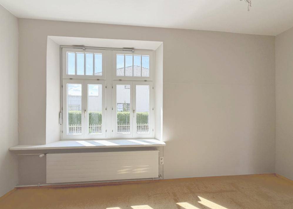 Leerer Raum mit großem Fenster und Heizkörper unter der Fensterbank.