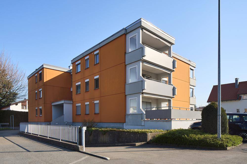 Mehrfamilienhaus mit orangefarbener Fassade, Balkonen und umliegenden Parkplätzen.