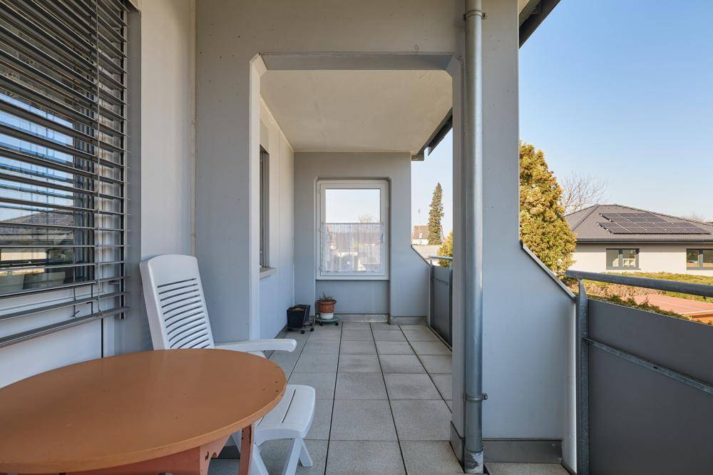 Überdachter Balkon mit Fliesenboden, Gartenmöbeln und Blick auf die Umgebung.