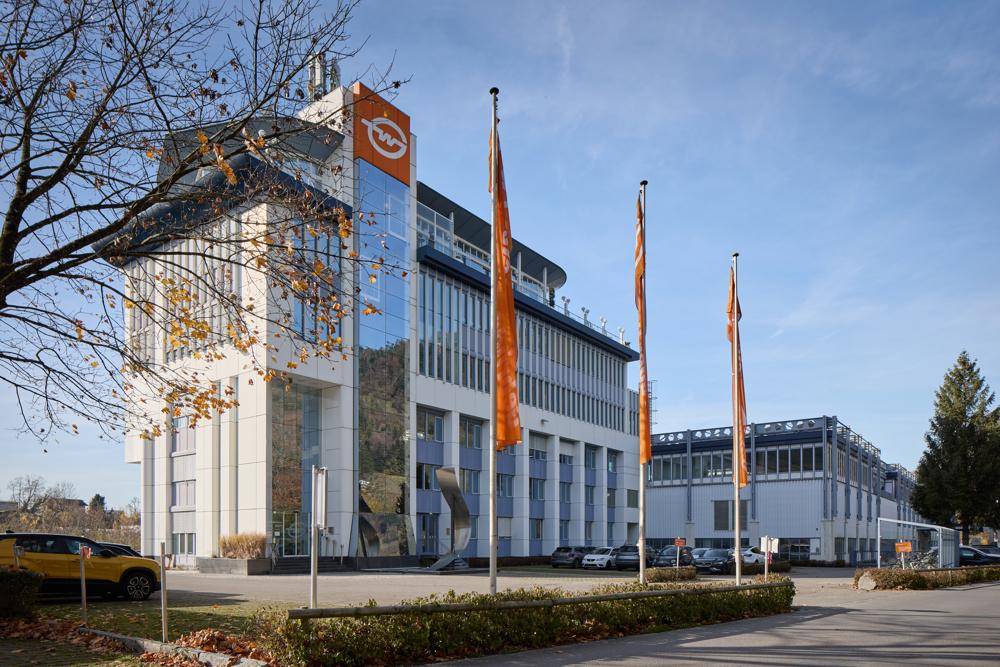 Ansicht eines modernen Bürokomplexes mit Glasfassade, Firmenflaggen und einem gepflegten Eingangsbereich.