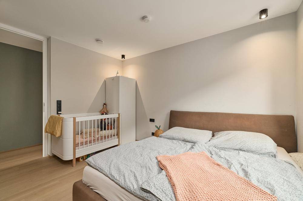 Helles Schlafzimmer mit Doppelbett, Babybett und Holzboden.