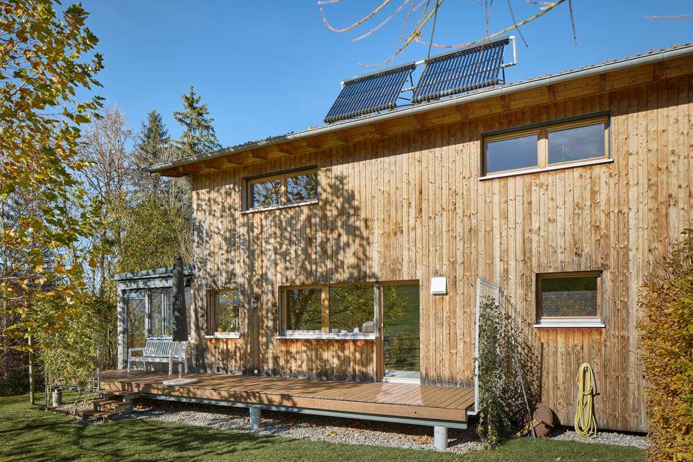 Modernes Holzhaus mit Solaranlage auf dem Dach und großer Holzterrasse.