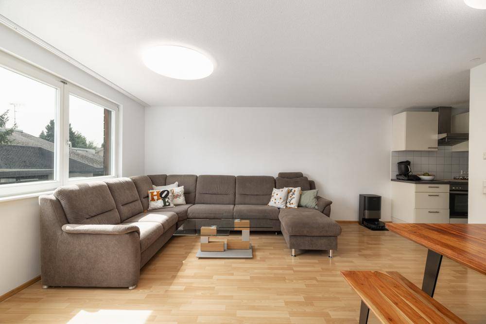 Heller Wohnbereich mit großem Ecksofa, Holzboden und offener Verbindung zur Küche.