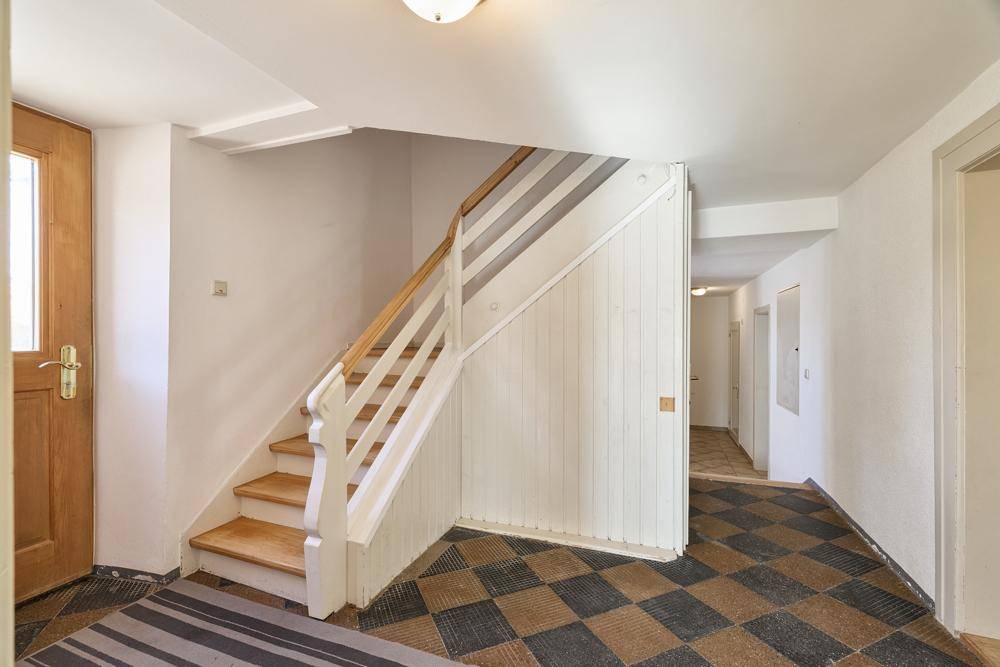 Eingangsbereich mit Holztreppe und gemustertem Bodenbelag, führt in den Flur.