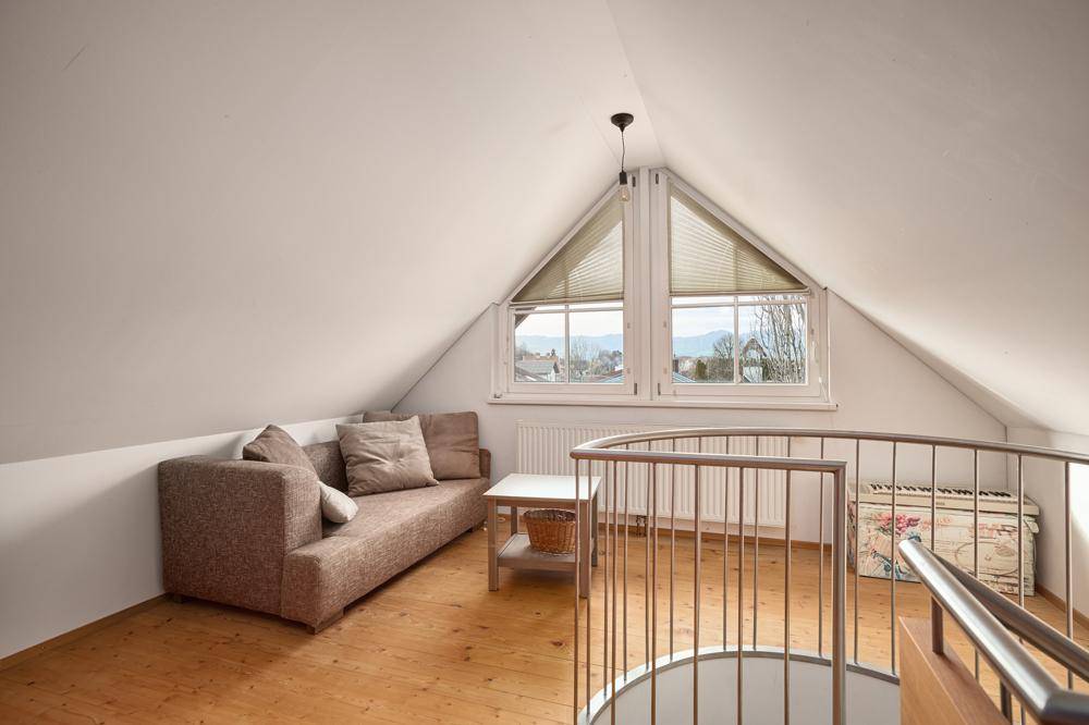 Gemütlicher Dachbodenbereich mit Sofa, Holzboden und Blick auf die umliegende Landschaft.