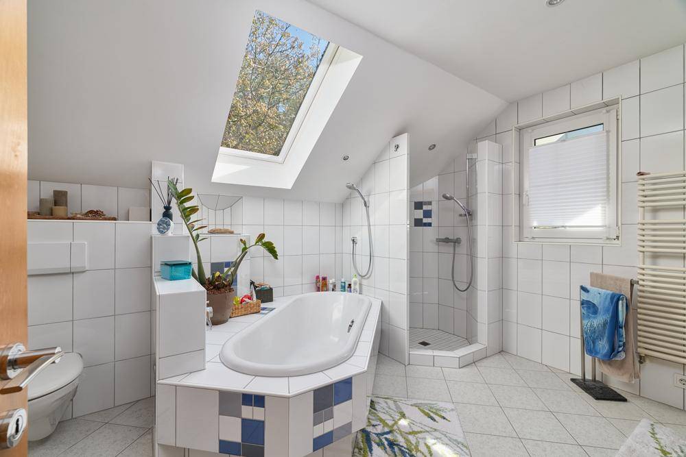 Helles Badezimmer mit Badewanne, Dusche, Dachfenster und weißen Fliesen in modernem Design.