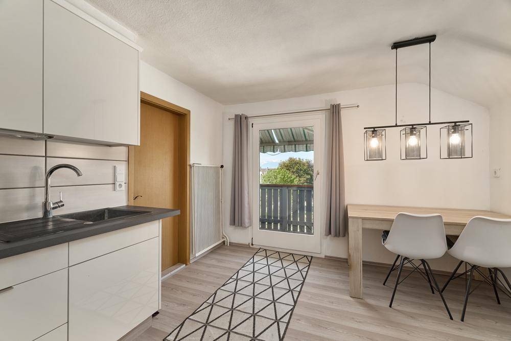Helle Küche mit weißen Schränken, Essbereich und Zugang zu einem Balkon.