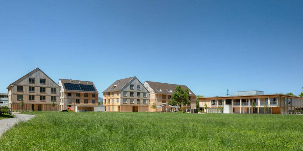 Moderne Holzgebäude in einer ländlichen Umgebung mit weiten Grünflächen unter blauem Himmel.