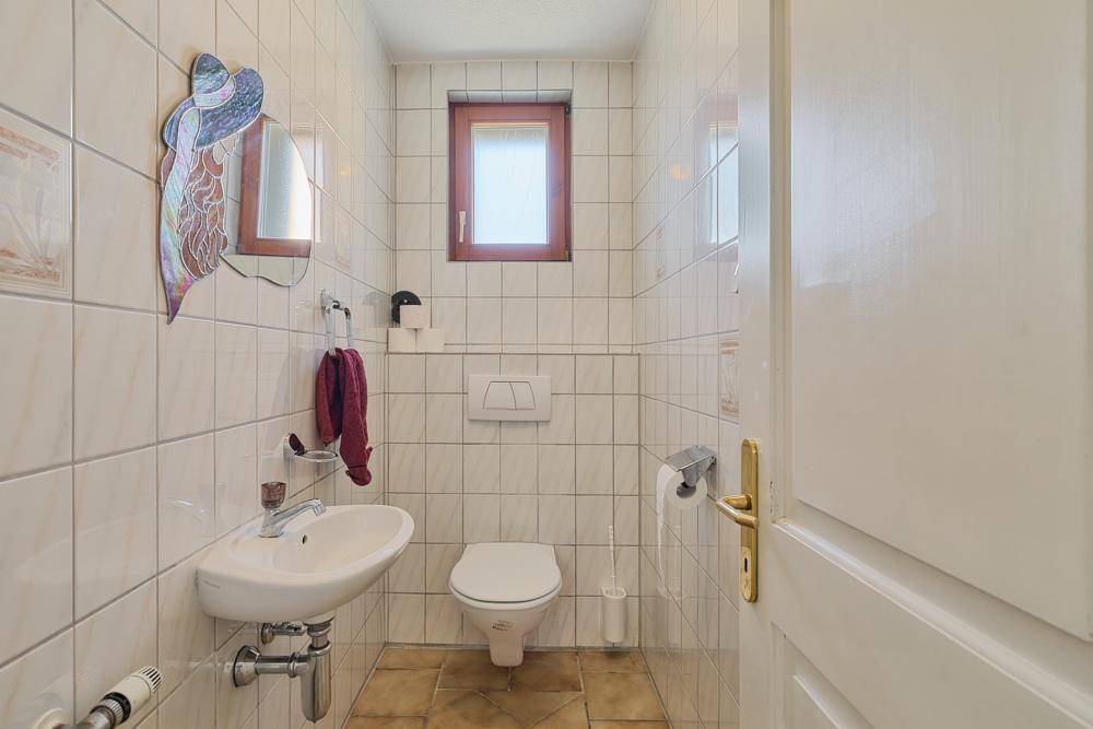 Kleines Gäste-WC mit wandhängendem WC, Waschbecken und Fenster.
