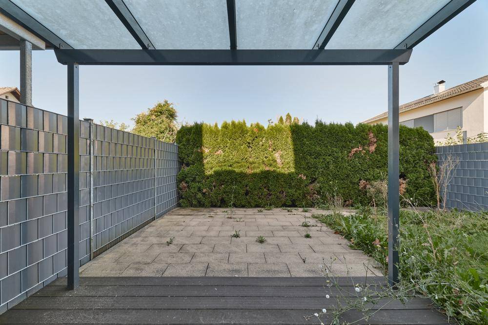 Außenbereich mit gepflasterter Terrasse, umgeben von einer hohen Hecke.