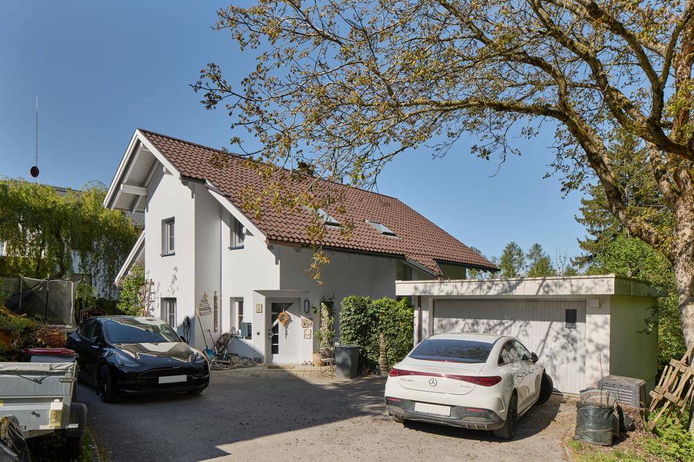 Freistehendes Einfamilienhaus mit Satteldach, Garage und mehreren Stellplätzen im Freien.