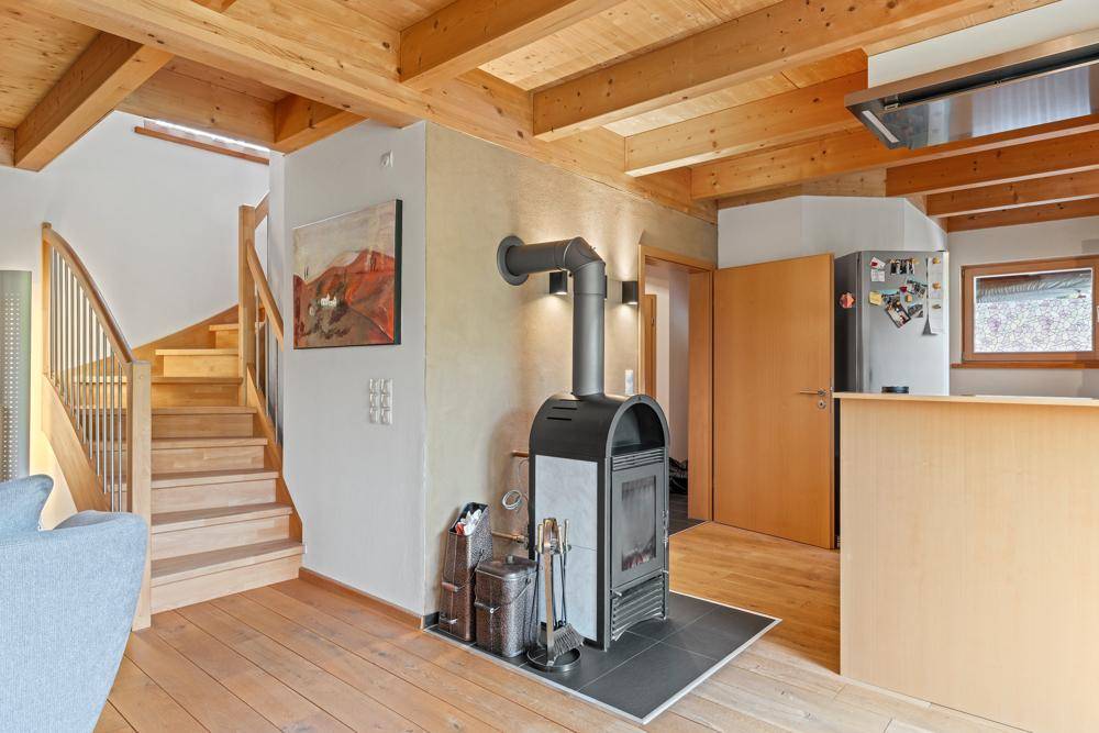 Offener Wohnbereich mit Kaminofen, Holztreppe und Zugang zur Küche.