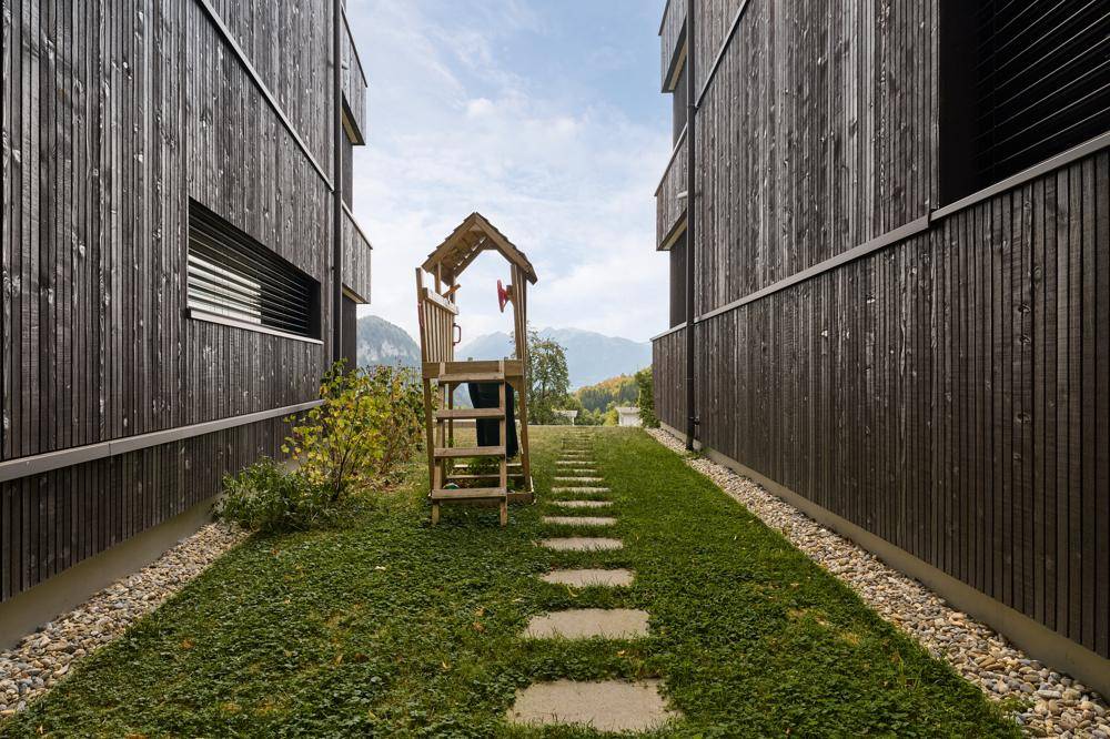 Gepflegter Gartenbereich zwischen zwei Gebäuden mit Spielhaus und Trittsteinen.