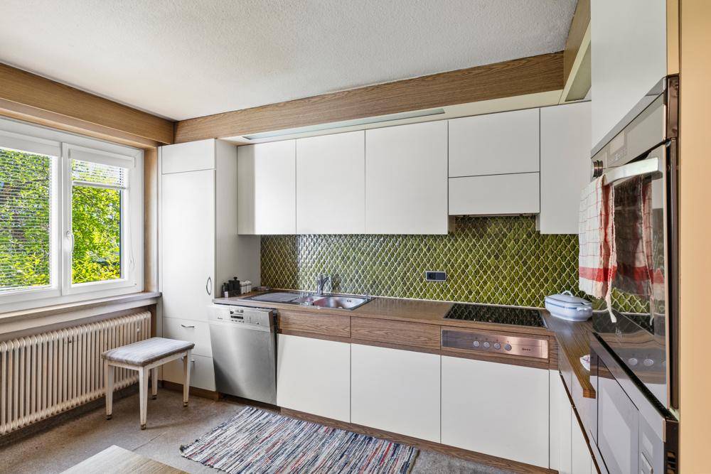 Küche mit weißen Schränken, Holz-Arbeitsplatten und grünen Fliesen als Spritzschutz.