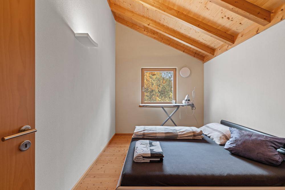 Einfaches Schlafzimmer mit Holzdachschräge, Doppelbett und Fenster mit Ausblick.