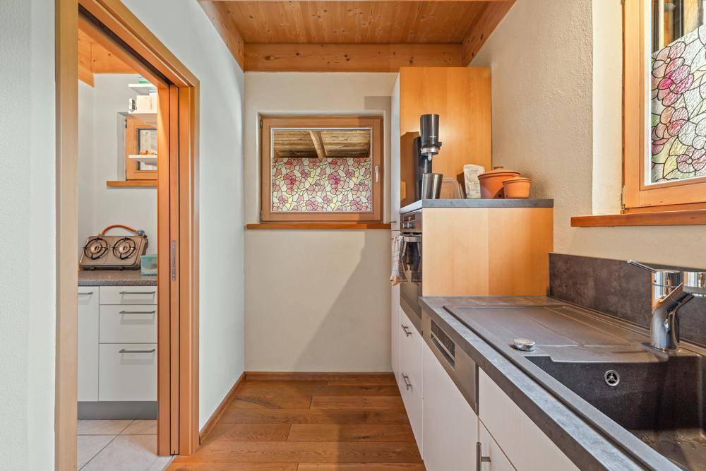 Schmale Küche mit Holzbalkendecke, Holzfußboden und Fenster mit Blick nach draußen.