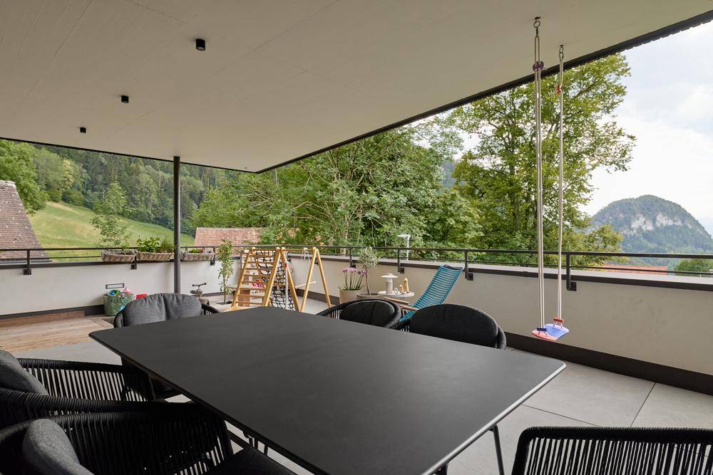 Weitläufiger Balkon mit Essbereich, Schaukel und Panoramablick auf die Berge und Natur.