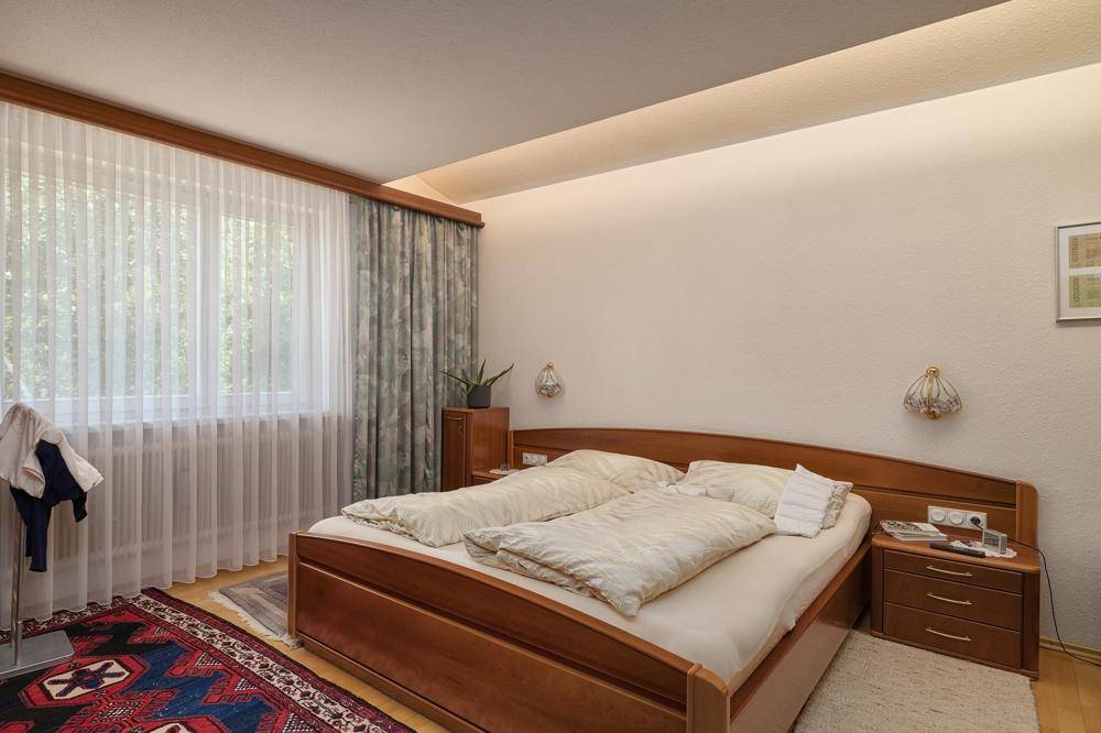 Gemütliches Schlafzimmer mit Doppelbett aus Holz und Vorhängen am Fenster.