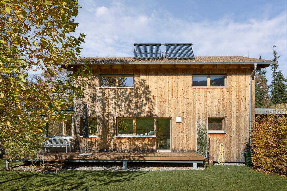 Ansicht des Holzhauses von hinten mit Solaranlage und weitläufigem Garten.
