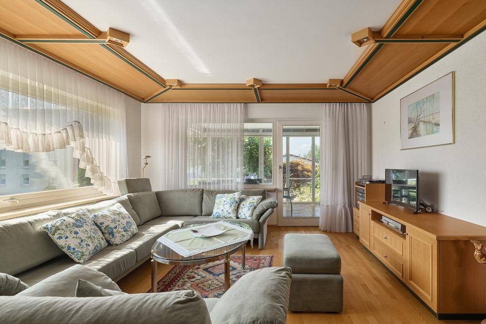 Helles Wohnzimmer mit Holzbalkendecke, bequemer Couch und Zugang zur Terrasse.