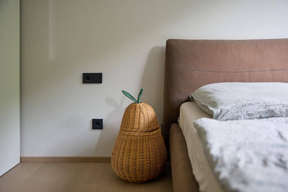 Gemütliches Schlafzimmer mit beigem Bettkopfteil und einem dekorativen Korb in Birnenform.