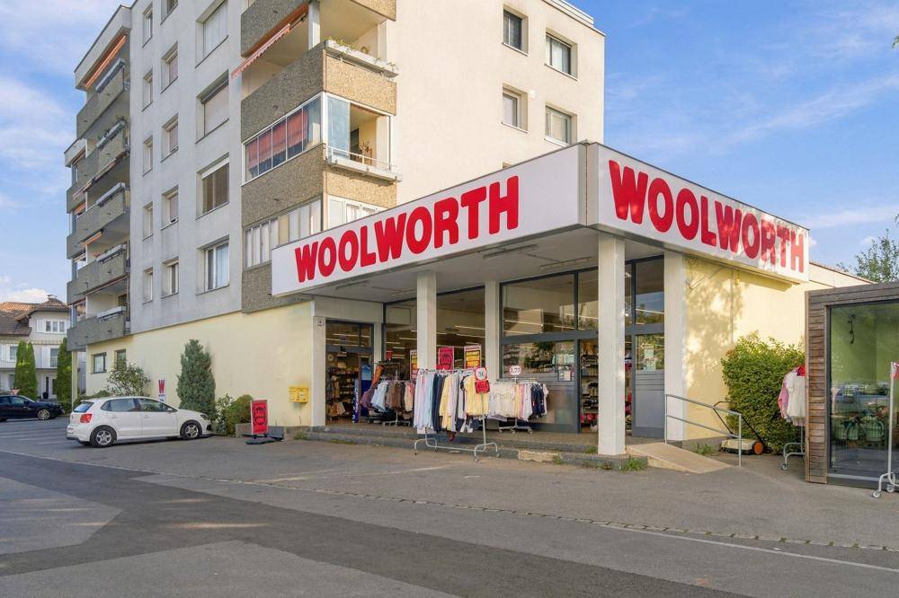 Ansicht des Woolworth-Eingangs mit dem darüber liegenden Wohngebäude und einem kleinen Parkplatz.
