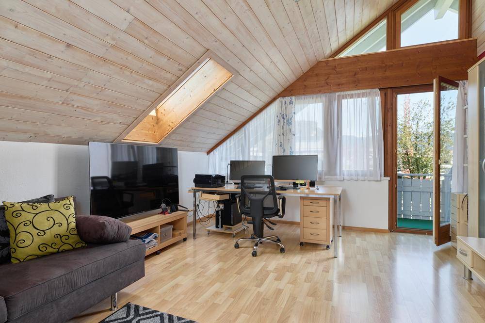 Geräumiger Wohnbereich im Dachgeschoss mit Holzbalkendecke, Dachfenster und Balkonzugang.