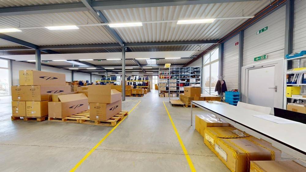 Weitläufiger Lagerbereich mit vielen Kartons, einem Arbeitstisch und Regalen im Hintergrund.