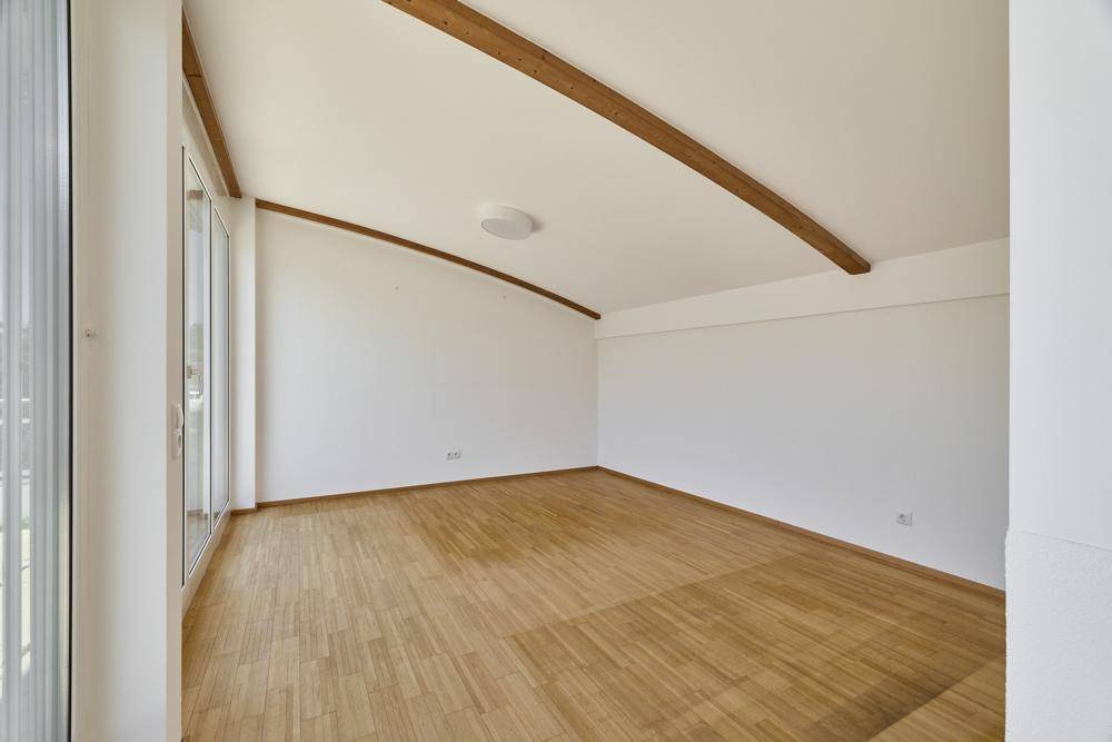 Geräumiges Zimmer im Dachgeschoss mit Holzboden, sichtbaren Holzbalken und Schrägdach.