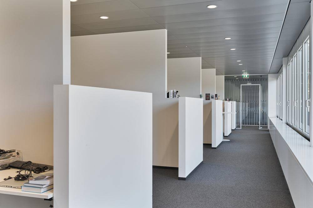 Offener Bürobereich mit einzelnen Arbeitskabinen, Teppichboden und großen Fenstern.