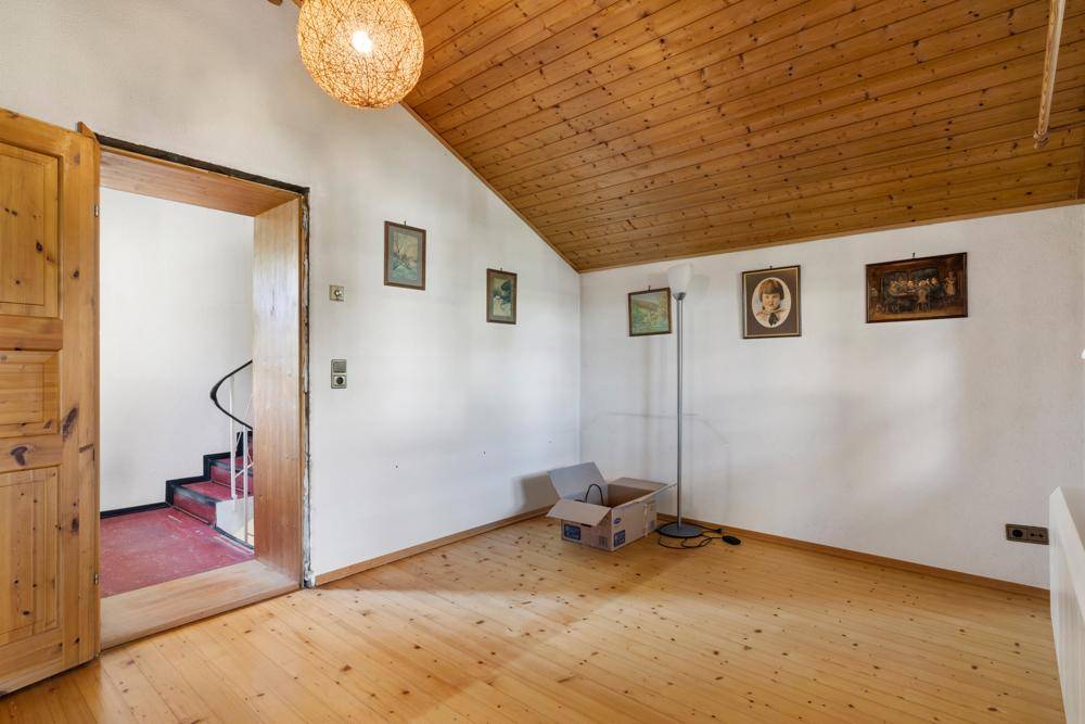Leerer Raum mit Holzdielenboden, Holzdecke und Zugang zu einer Wendeltreppe.