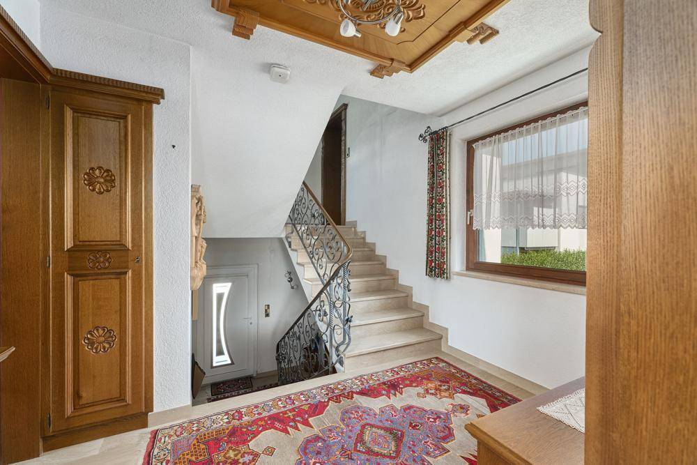 Eingangsbereich mit Steintreppe, schmiedeeisernem Geländer und Holztür im traditionellen Stil.