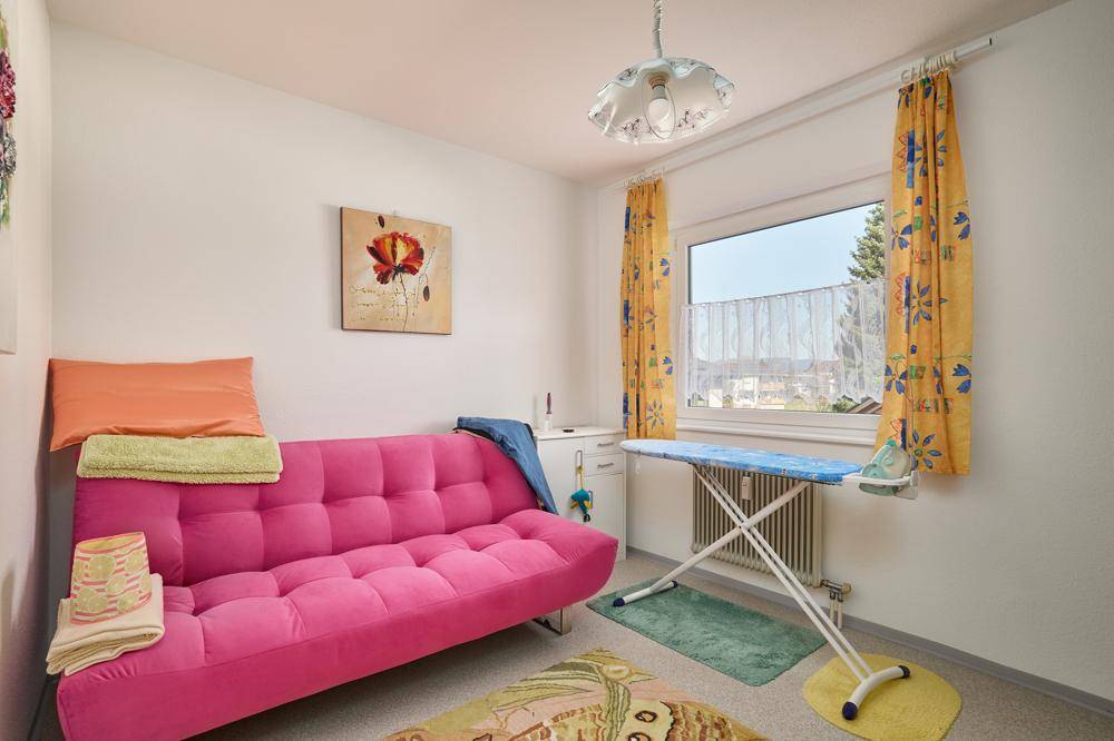 Vielseitiger Raum mit Sofa, Bügelbrett und Fenster, ideal als Gäste- oder Hauswirtschaftszimmer.