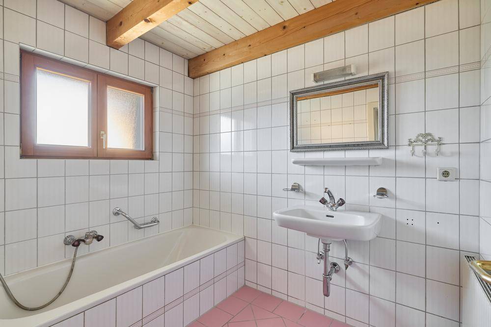 Badezimmer mit Badewanne, Waschbecken, weißen Fliesen und rosa Boden.