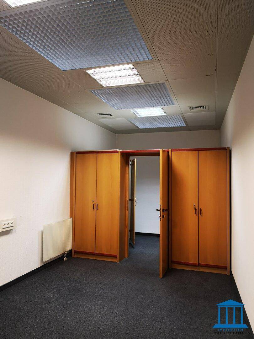 Büroflur mit Teppichboden und zwei Holzschränken, führt zu weiteren Räumen im Gebäude.