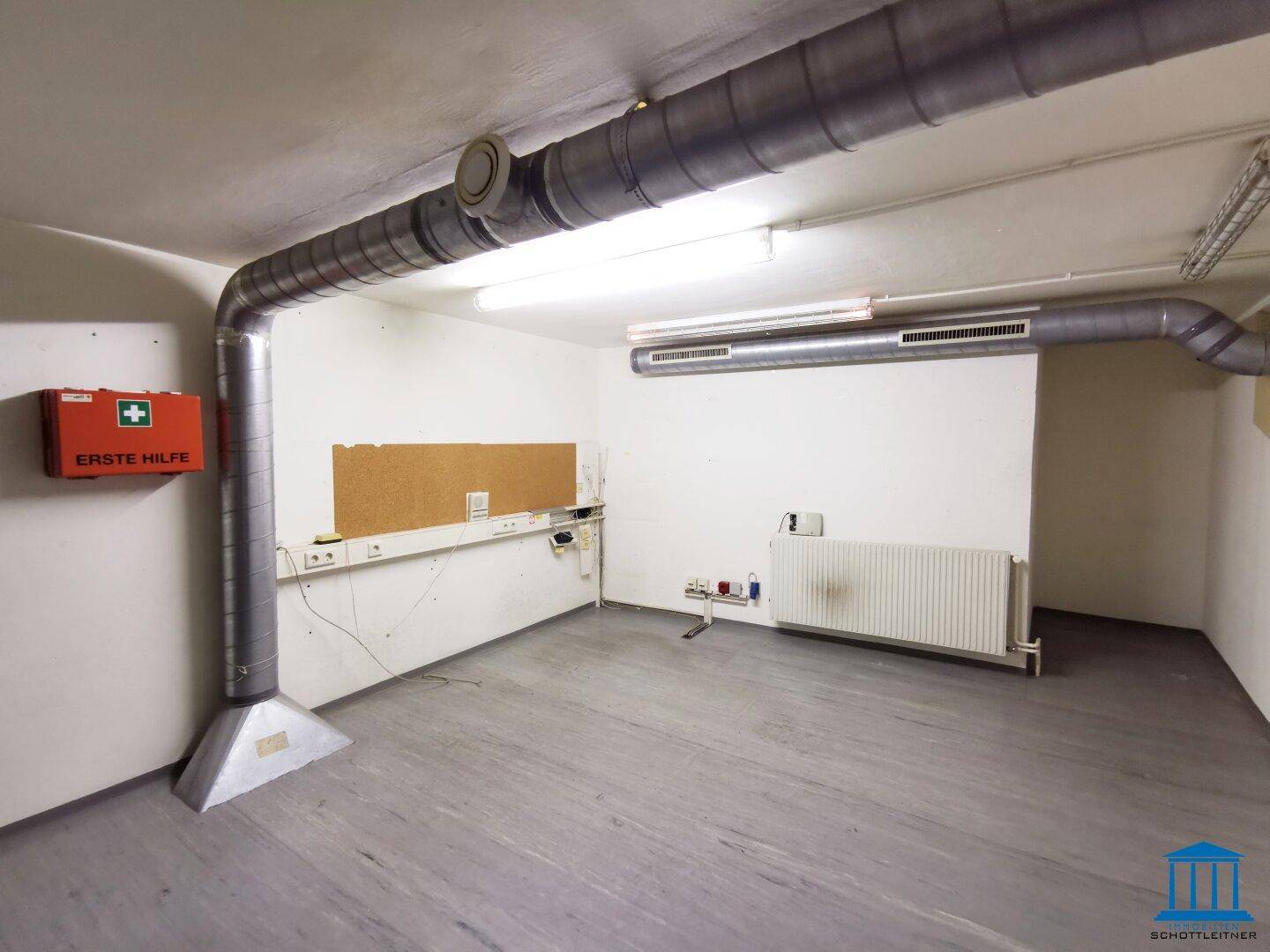 Funktionaler Hauswirtschaftsraum mit sichtbaren Lüftungsrohren, Heizkörper und Erste-Hilfe-Kasten.