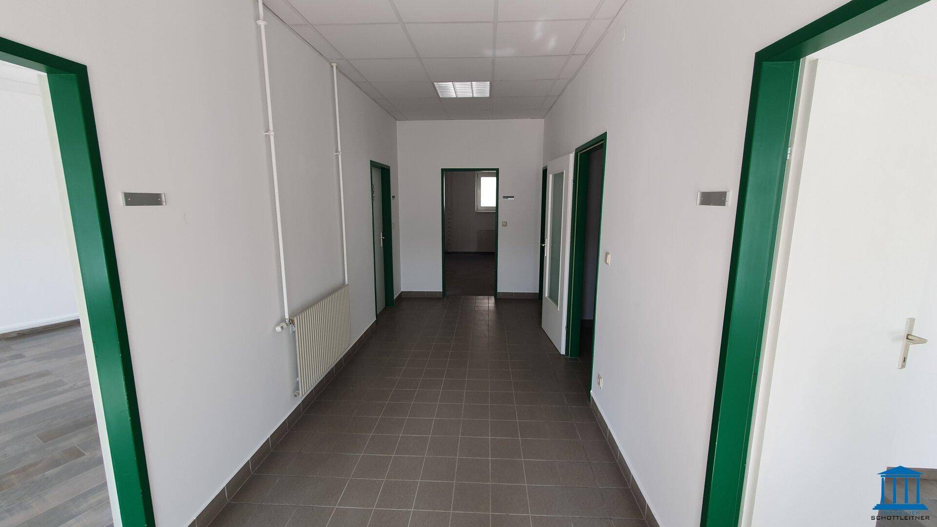 Langer Flur mit Fliesenboden, weißen Wänden und mehreren Türen, führt zu verschiedenen Räumen.